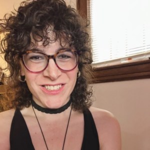 headshot of a white woman with dark curly hair wearing eyeglasses 