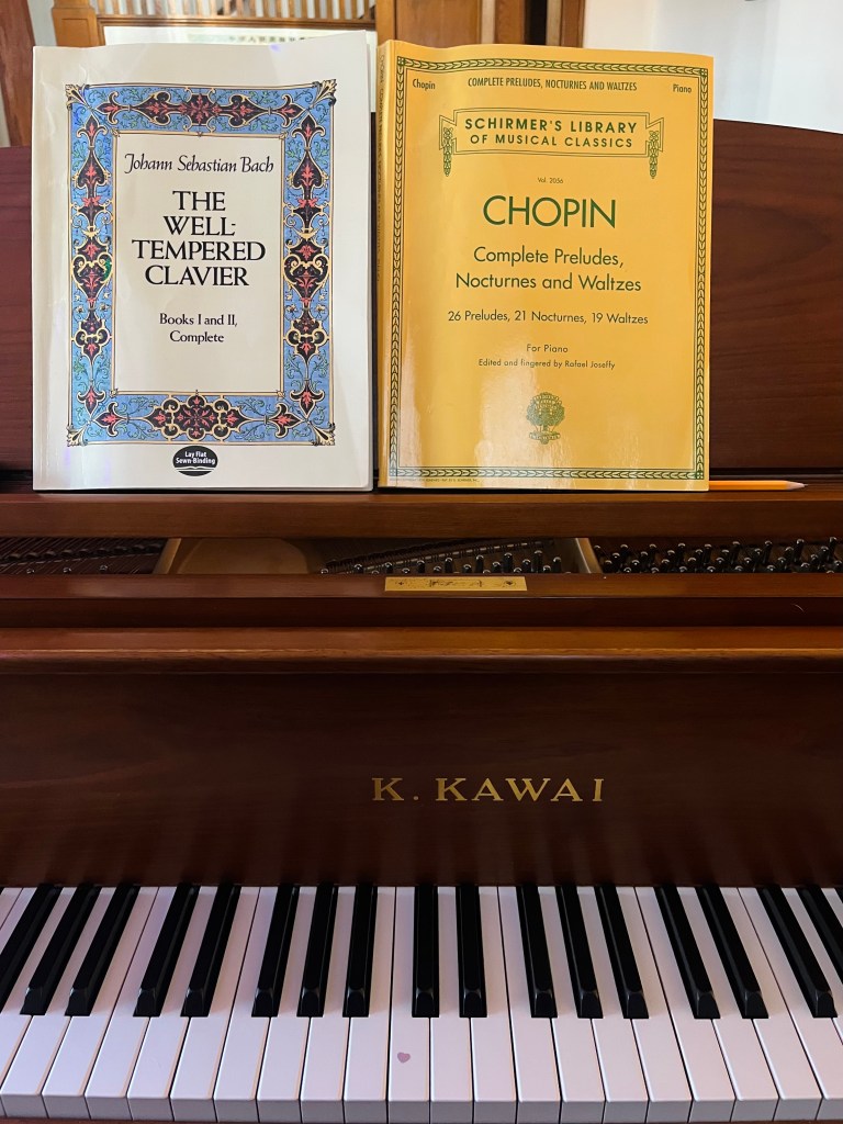 A Kawai baby grand piano with two piano books on the music stand: Johann Sebastian Bach's The Well-Tempered Clavier and a collection of Chopin Preludes and Nocturnes 